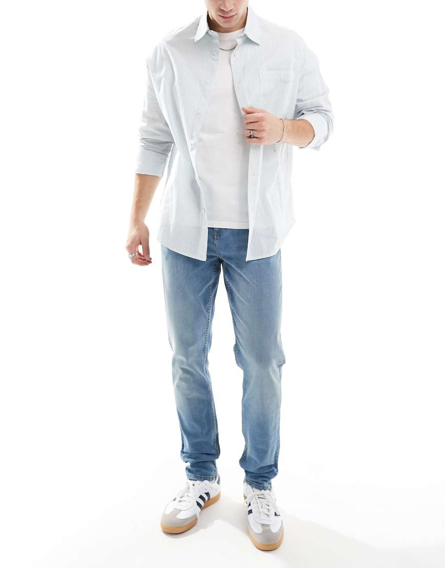 ASOS DESIGN - Eng geschnittene Jeans in mittelblauer Waschung mit gelber Tönung von ASOS DESIGN