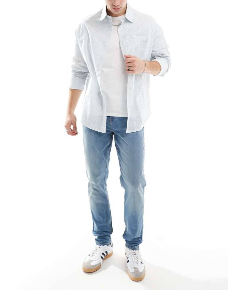 ASOS DESIGN - Eng geschnittene Jeans in mittelblauer Waschung mit gelber Tönung von ASOS DESIGN