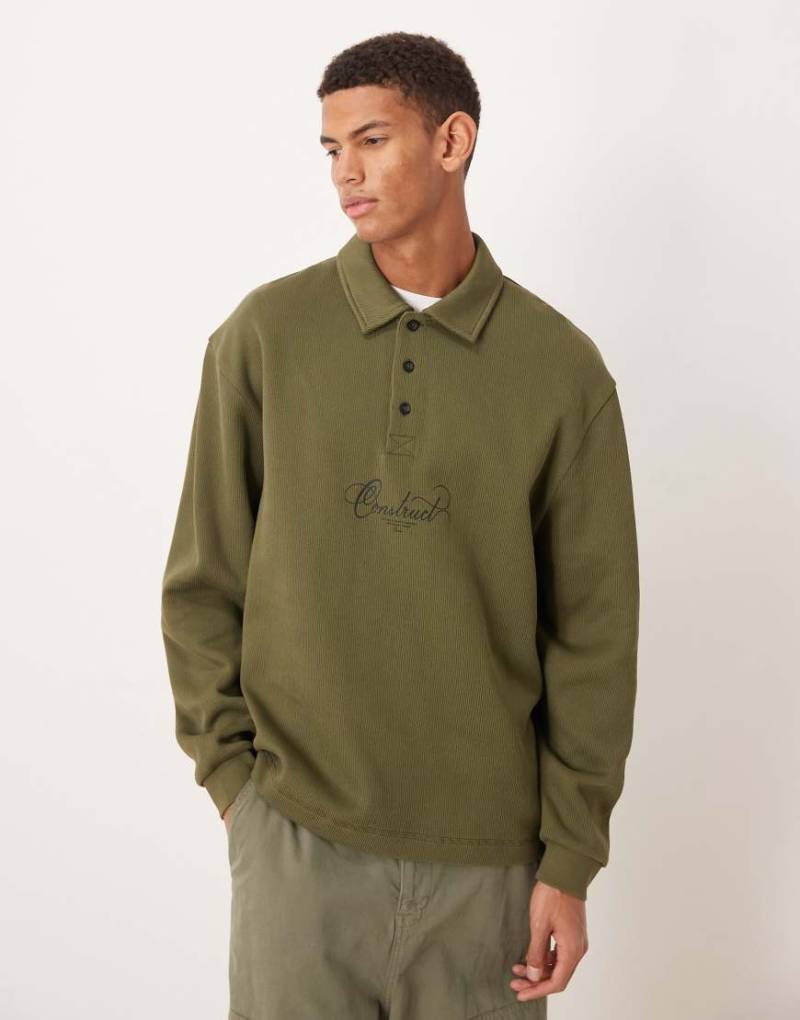 ASOS DESIGN - Geripptes Polo-Sweatshirt in Khaki mit Textprint und gewebtem Etikett-Grün von ASOS DESIGN