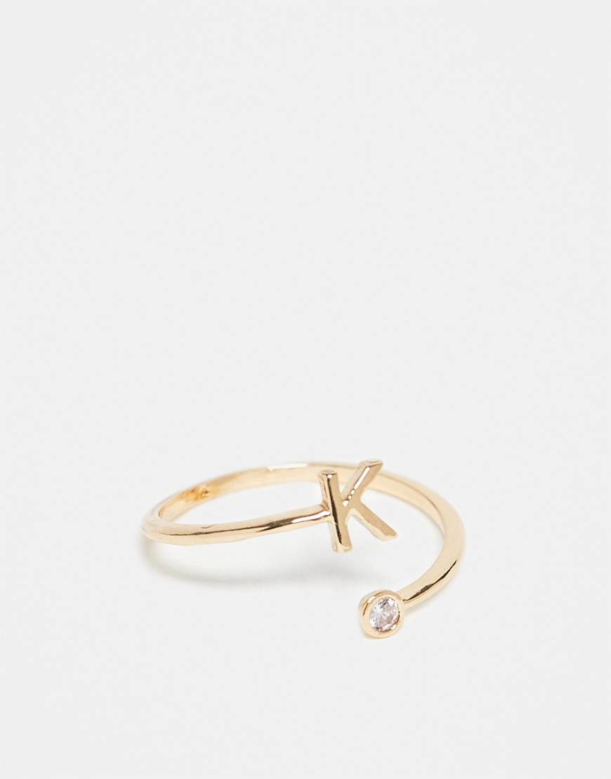 ASOS DESIGN - Goldfarbener Ring mit Wickeldesign, Zirkoniabesatz, „K"-Initiale und Geschenkbeutel von ASOS DESIGN
