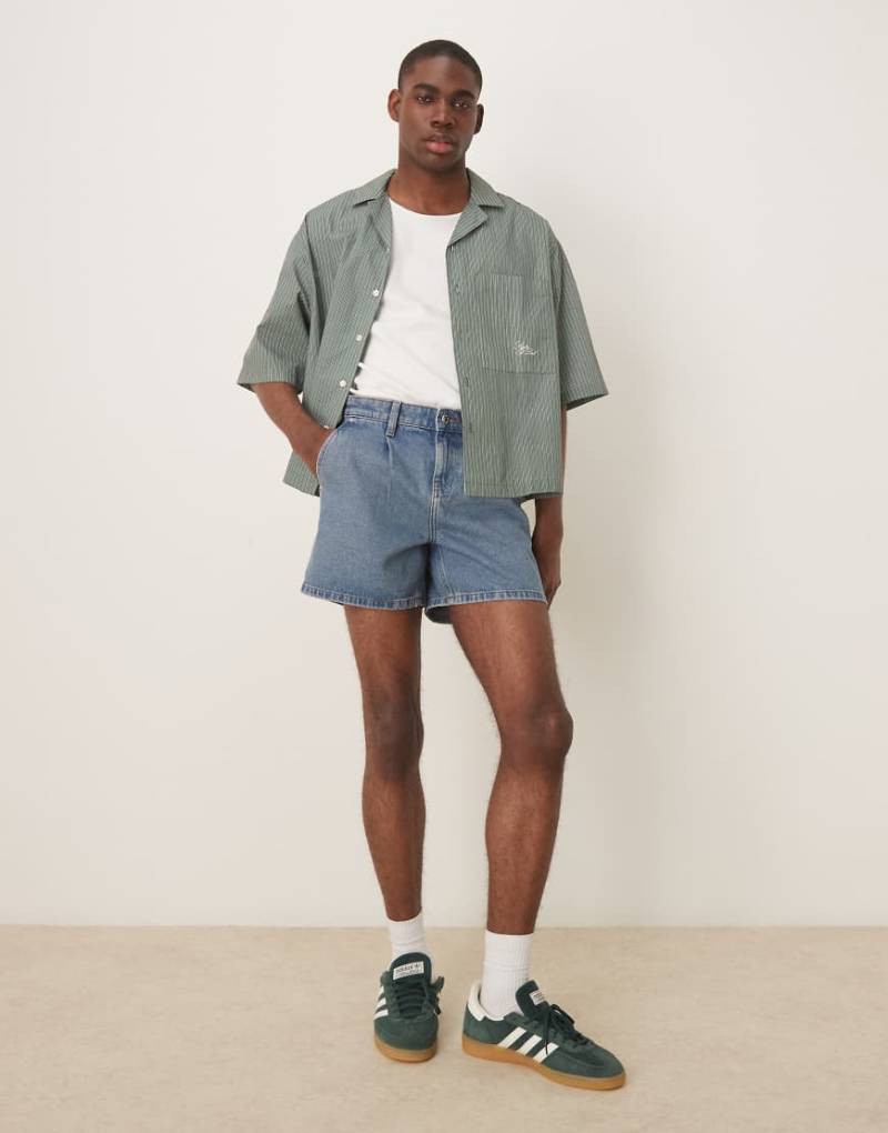 ASOS DESIGN - Schmal geschnittene, kurze Jeans-Shorts in mittelblauer Waschung mit Bundfalten von ASOS DESIGN
