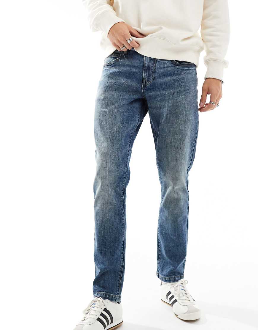 ASOS DESIGN - Schmal geschnittene, überfärbte Jeans in verwaschenem Mittelblau von ASOS DESIGN