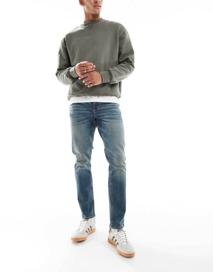 ASOS DESIGN - Schmal geschnittene, überfärbte Jeans in verwaschenem Mittelblau von ASOS DESIGN