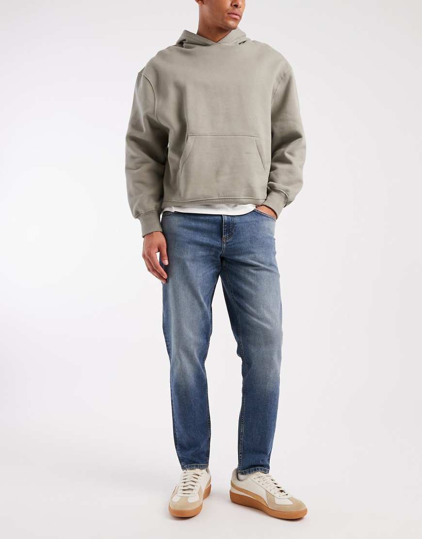 ASOS DESIGN - Schmal zulaufende Jeans in mittelblauer Waschung mit Farbstich von ASOS DESIGN