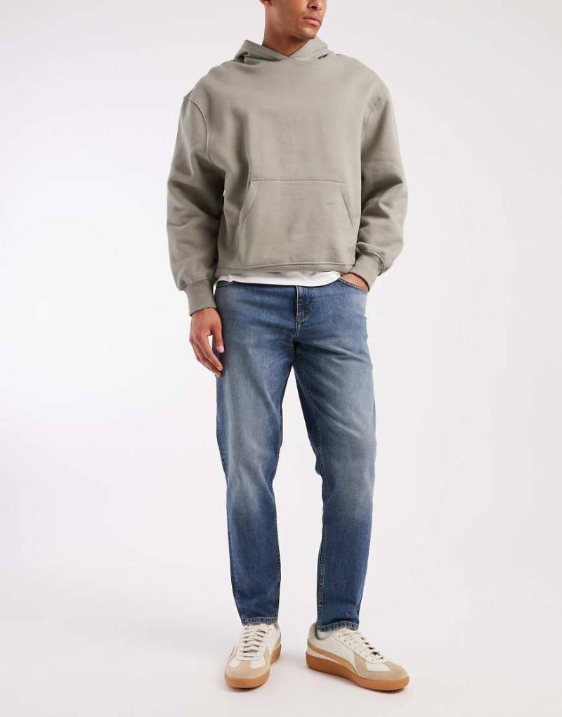 ASOS DESIGN - Schmal zulaufende Jeans in mittelblauer Waschung mit Farbstich von ASOS DESIGN