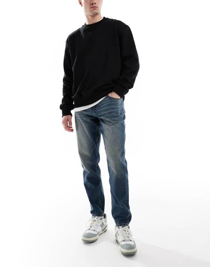 ASOS DESIGN - Schmal zulaufende Jeans in verwaschenem Dunkelblau mit Vintage-Tönung von ASOS DESIGN