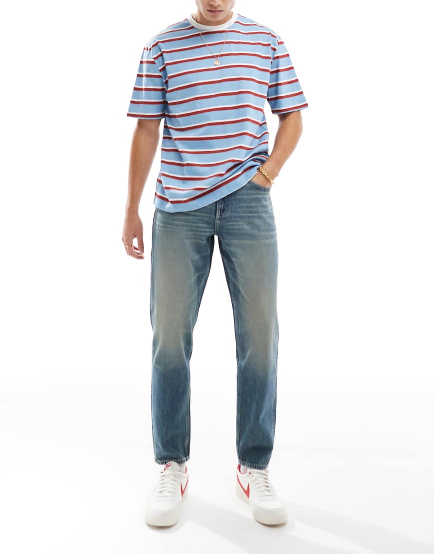 ASOS DESIGN - Schmal zulaufende Jeans in verwaschenem Mittelblau mit Vintage-Farbstich von ASOS DESIGN