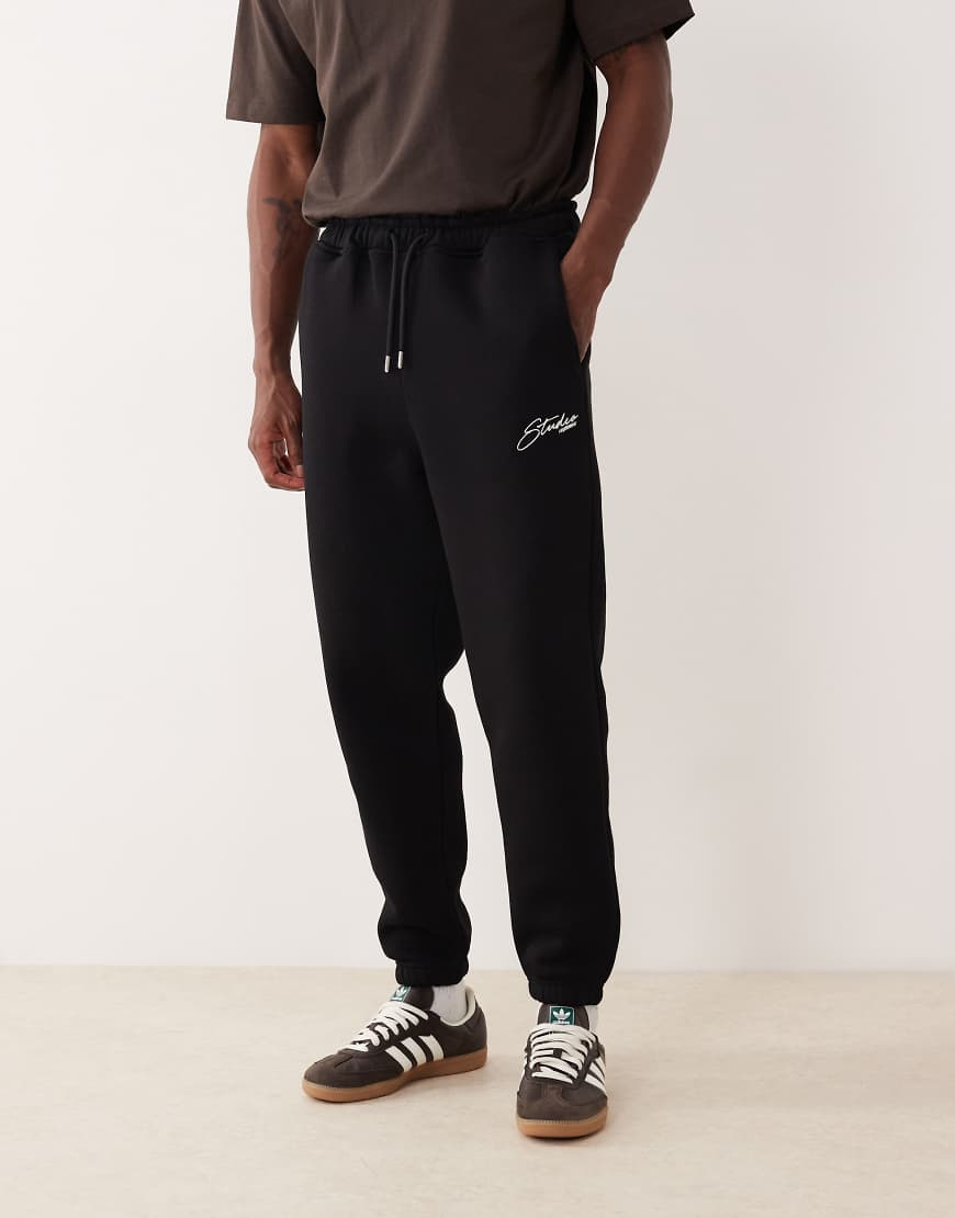 ASOS DESIGN - Schmal zulaufende Jogginghose in Schwarz mit aufgesticktem Motiv von ASOS DESIGN