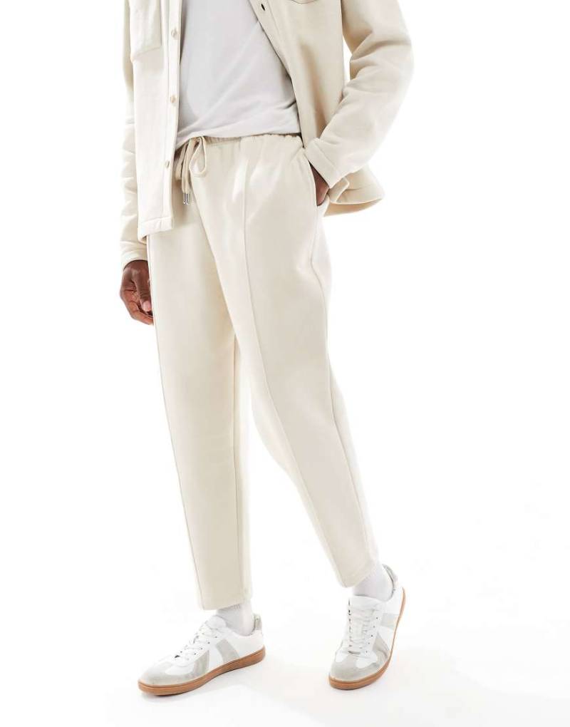 ASOS DESIGN - Schmal zulaufende Jogginghose in Steinbeige mit festem Saum und Falten-Neutral von ASOS DESIGN