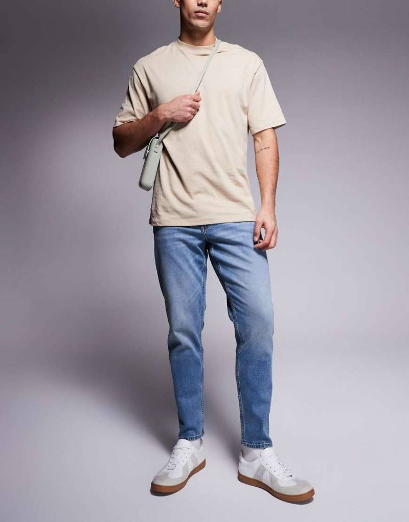 ASOS DESIGN - Schmal zulaufende Stretch-Jeans in mittelblauer Waschung mit Vintage-Tönung von ASOS DESIGN