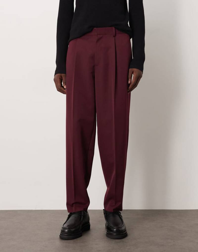 ASOS DESIGN - Elegante, schmal zulaufende Oversize-Hose in Burgunderrot mit Bundfalten und elastischem Bund von ASOS DESIGN