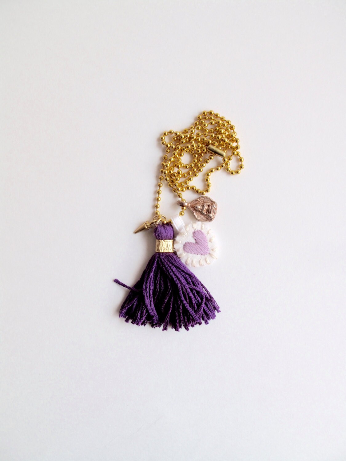 Bettelkette Mit Besticktem Lavendelfarbenem Herz, Buddha-Charme Und Violetter Quaste An Einer Langen Goldfarbenen Kugelkette Bettelkette Mit Besticktem Lavendelfarbenem Herz, Buddha-Charme Und Violetter Quaste An Einer Langen Goldfarbenen Kugelkette von AnAstridEndeavor