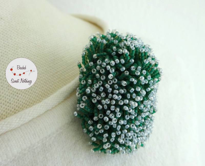 Moosbrosche in Trendfarbe Grün. Auf Dunkelgrünem Grund Sitzen Hunderte Grüner Stengel Mit Perlmuttfarbenen Perlchen Als Abschluss von BeadedSweetNothings