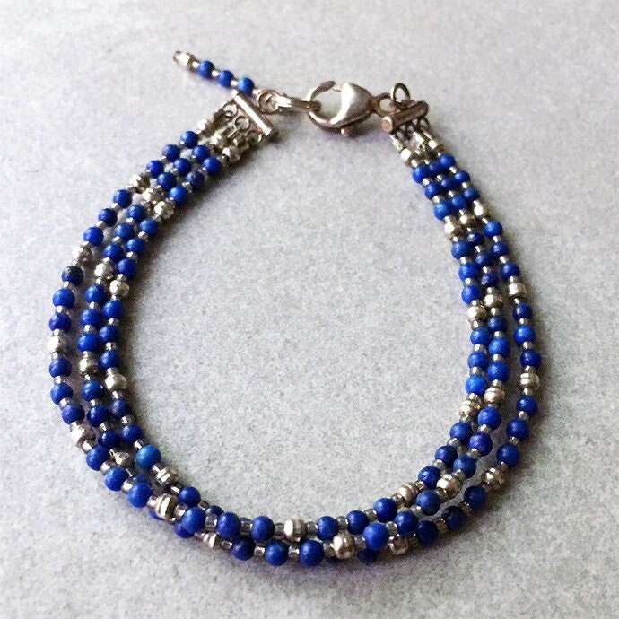 Drei Stränge Aus Blauen Lapis-Rounds Und Diamond Cut Sterling Silber-Rounds Sind Ein Selbststapelndes Armband Mit Einem Baumeln Am Drei Stränge Aus Blauen Lapis-Rounds Und Diamond Cut Sterling Silber-Rounds Sind Ein Selbststapelndes Armband Mit Einem Baumeln Am von BeadsByBurch