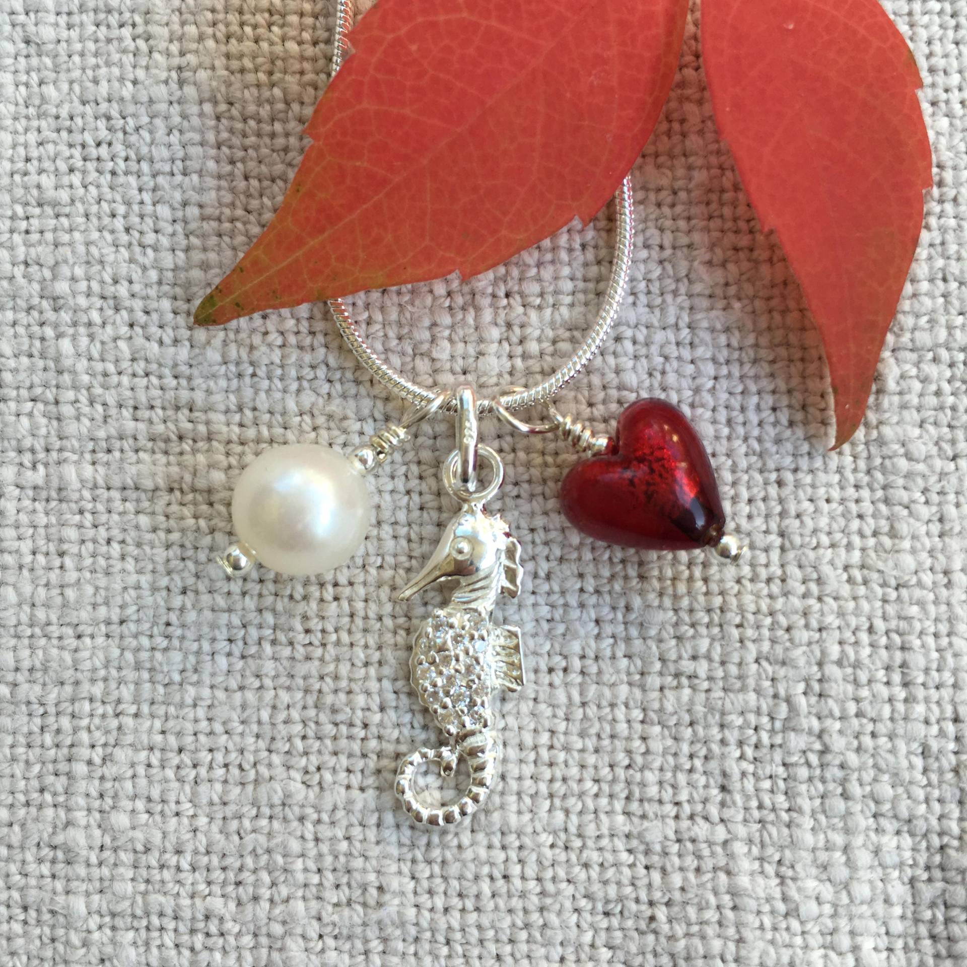 Diana Ingram Drei Bettelkette Aus Sterling Silber Mit Rotem Muranoglas Herz, Seepferdchen, Weißer Perle Und Schlangenkette Diana Ingram Drei Bettelkette Aus Sterling Silber Mit Rotem Muranoglas Herz, Seepferdchen, Weißer Perle Und Schlangenkette von DianaIngramJewellery