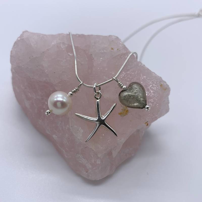 Diana Ingram Drei Bettelkette in Sterling Silber Mit Grauem Muranoglas Herz, Seestern, Weißer Perle Und Schlangenkette Diana Ingram Drei Bettelkette in Sterling Silber Mit Grauem Muranoglas Herz, Seestern, Weißer Perle Und Schlangenkette von DianaIngramJewellery