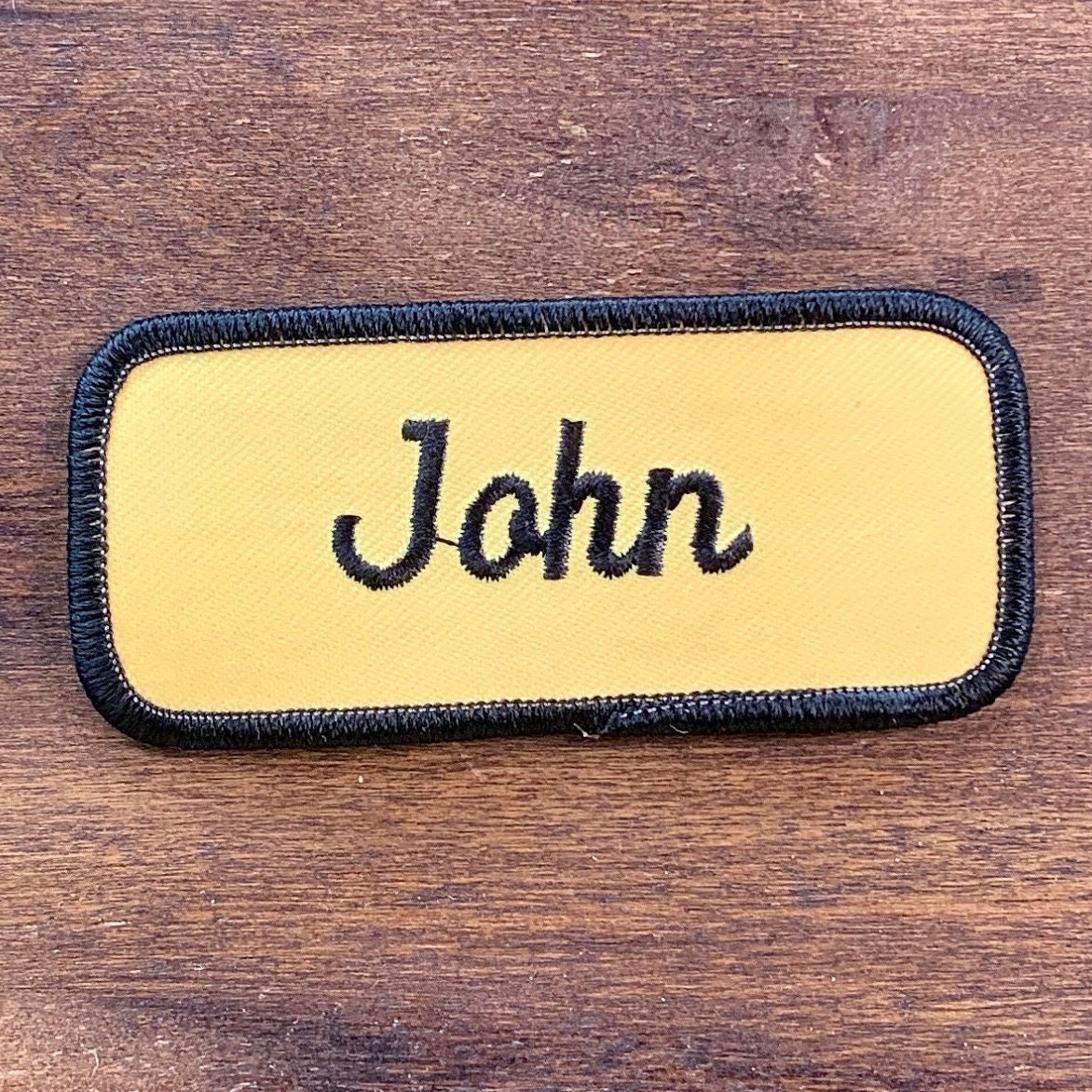 John. Ein Gelber Arbeitsshirt Aufnäher Mit Der Aufschrift "John" in Schwarzer Schrift Schwarzem Rand von HeydayRetroMart