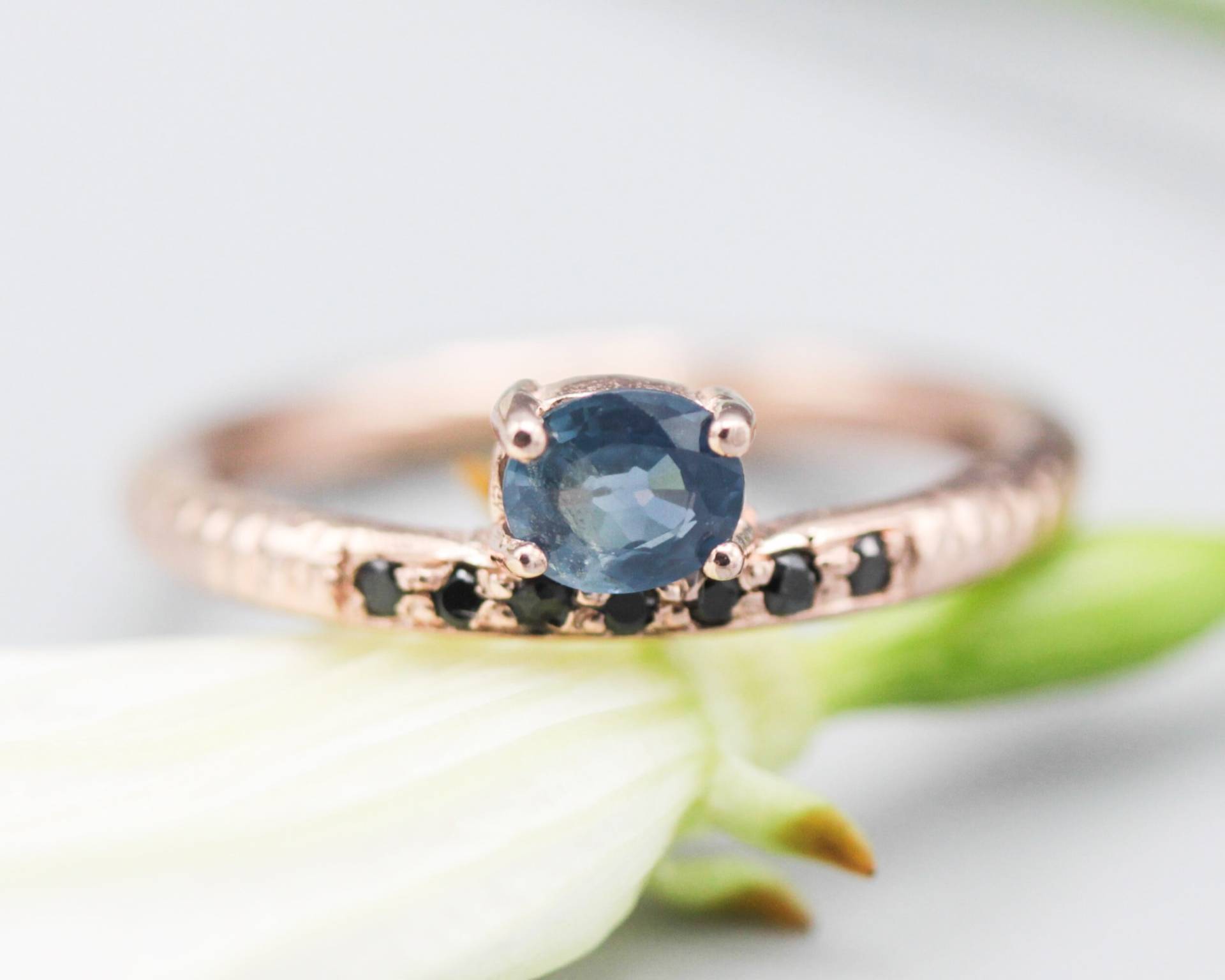 Ovaler Facettierter Blauer Saphir Ring in Krappenfassung Mit Winzigen Schwarzen Spinell Auf 14K Rose Gold Textur Design Band von MetalStudioJewelry