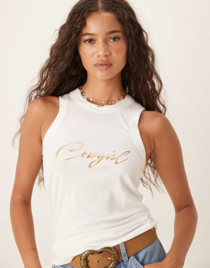 Never Fully Dressed - Geripptes Tanktop in Weiß mit „Cowgirl"-Aufschrift in Metallic-Gold Never Fully Dressed - Geripptes Tanktop in Weiß mit „Cowgirl"-Aufschrift in Metallic-Gold von Never Fully Dressed