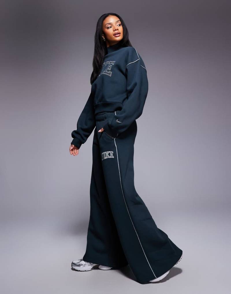 Nike - Jogginghose in Dunkelgrün mit weitem Bein und Retro-Logo Nike - Jogginghose in Dunkelgrün mit weitem Bein und Retro-Logo von Nike