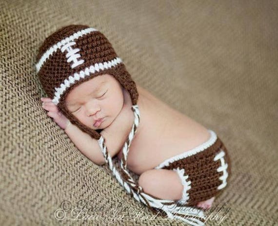 Handgemachtes Häkel-Baby-Fußball-Set Mit Ohrflap-Mütze Und Zöpfen Windelbezug. Perfektes Baby Shower Geschenk Oder Neugeborenen Foto Requisite von OhSoVeryKnotty