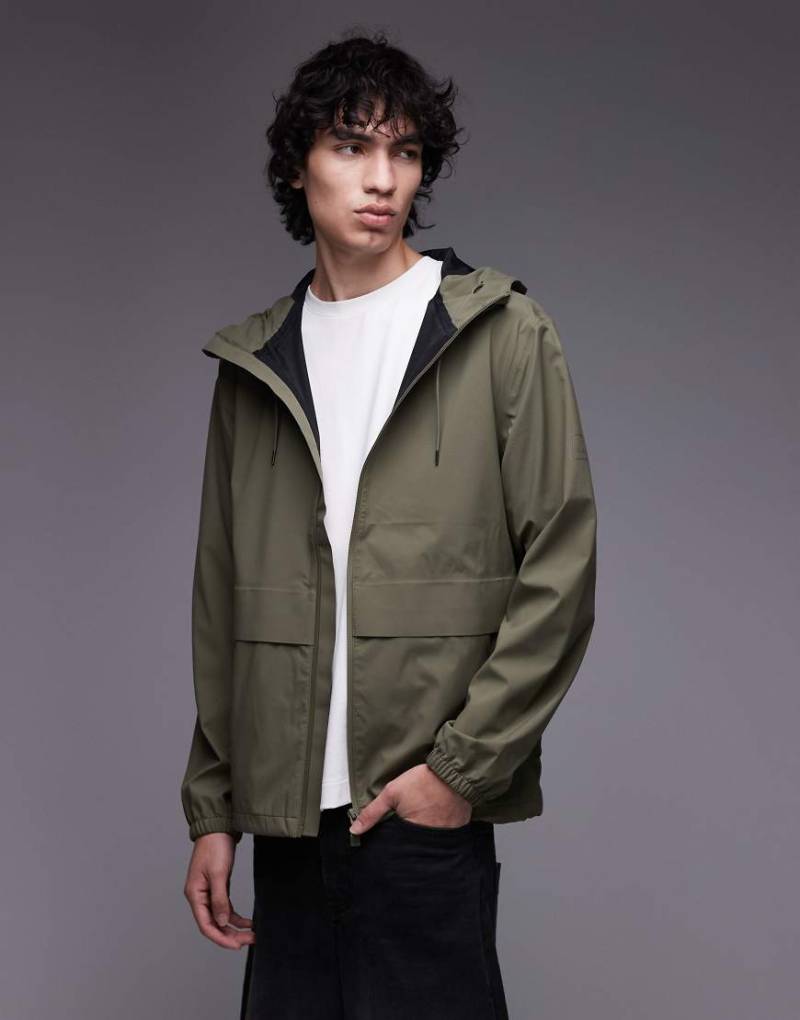 Rains - 12420 Suva - Wasserdichte Hardshell-Jacke in Khaki mit Reißverschluss-Grün Rains - 12420 Suva - Wasserdichte Hardshell-Jacke in Khaki mit Reißverschluss-Grün von Rains