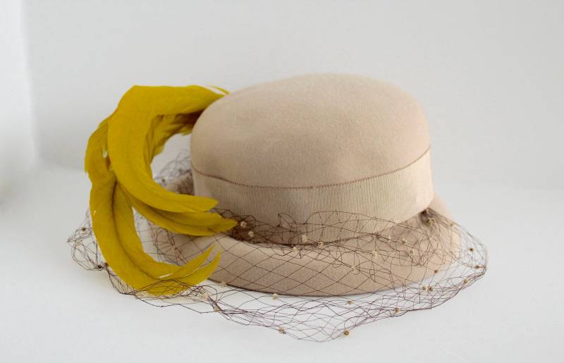 1940Er Beigefarbener Bonnet-Hut Mit Ripsbandband, Braunem Netzschleier Und Leuchtend-Gelb-Grünen Federn Modelle Von Mathilde Bodies Lee 1940Er Beigefarbener Bonnet-Hut Mit Ripsbandband, Braunem Netzschleier Und Leuchtend-Gelb-Grünen Federn Modelle Von Mathilde Bodies Lee von WesternWallflowers