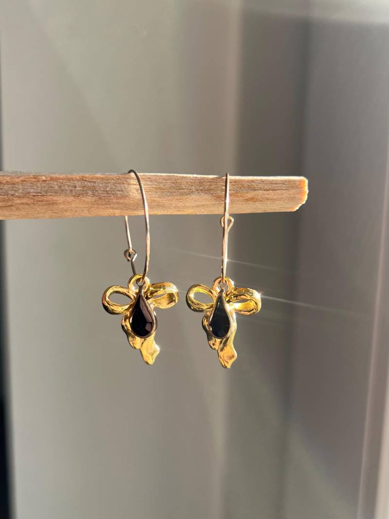 Creolen in Gold Aus Edelstahl Mit Goldener Schleife Und Schwarzem Tropfenförmigen Charm von ellsandemms