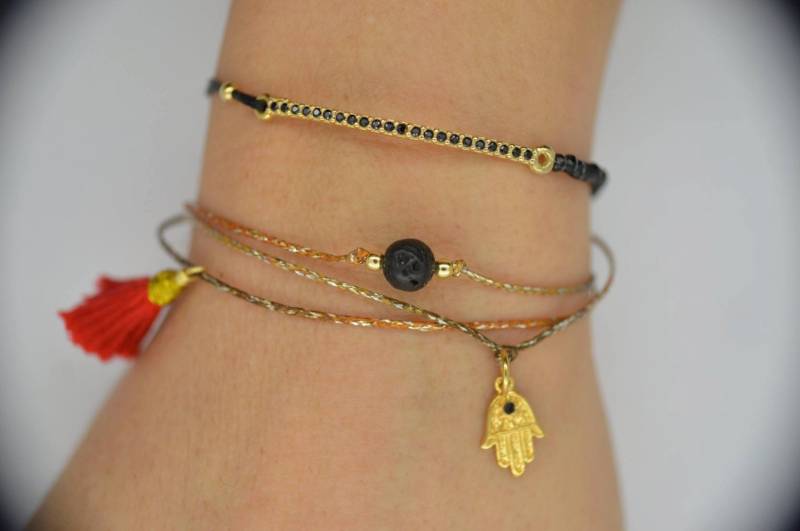 Gewachstes Armband Aus Metallisch Gewachsten Garnen Mit Einem Vulkangestein Und Einer Handgemachten Roten Quaste von georgiaroidou